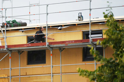 Symbolbild Baustelle: Ein Handwerker mit Zollstock in der linken Hand markiert etwas mit der rechten Hand an einer Außenwand